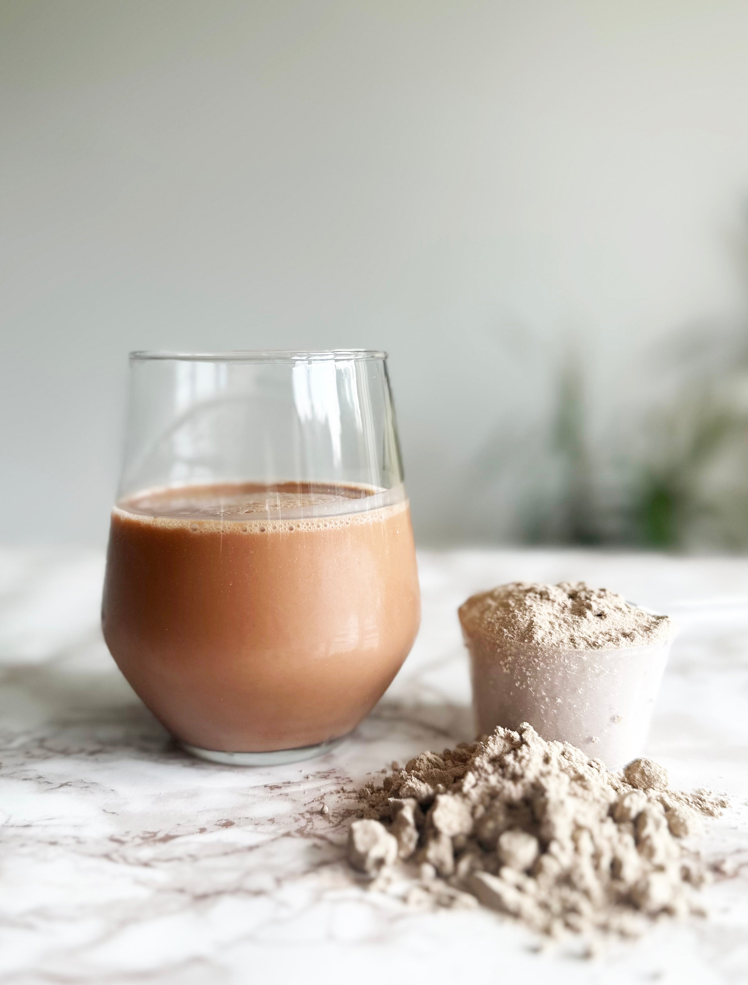 Glass of chocolate oat milk with powdered cocoa on a white surface